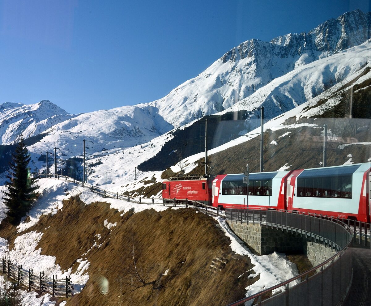 A red Matterhorn Gotthard Bahn Glacier Express train curving along a snowy mountainside in winter