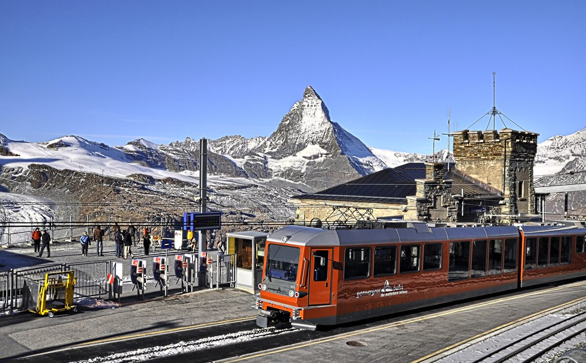 Gornergrat station with a red train, the Matterhorn and snowy ground on a sunny winter day