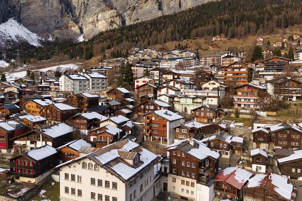 Wooden chalets and hotels of Leukerbad village in winter, with a rock wall rising behind