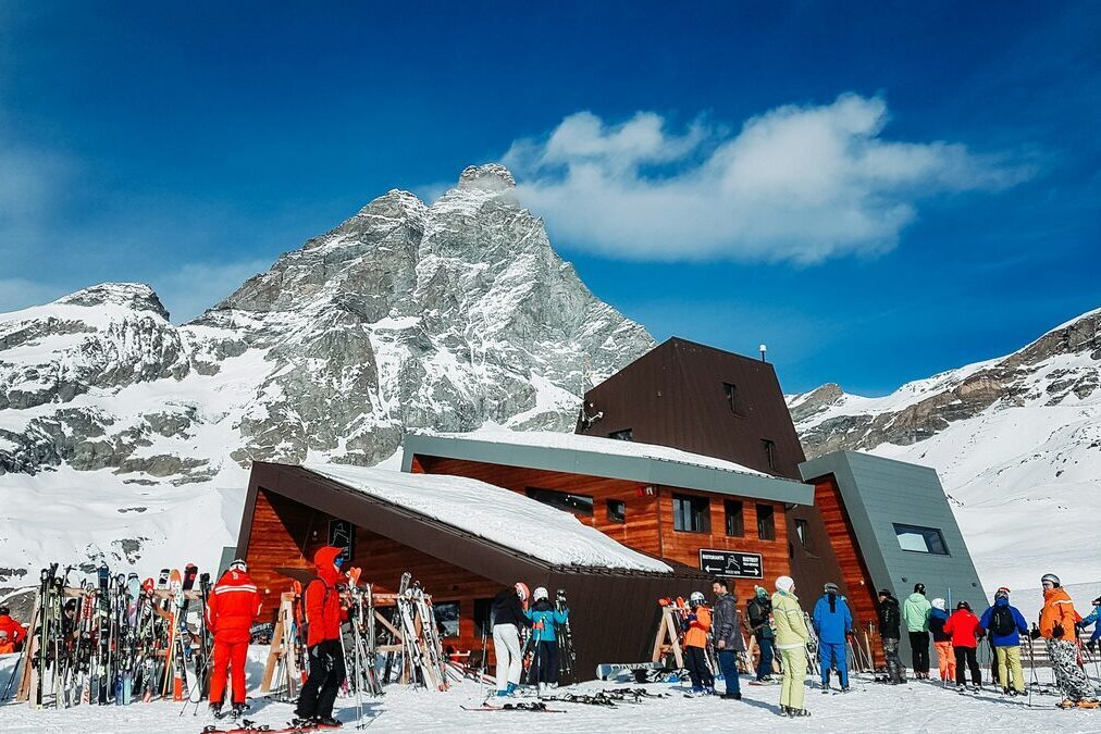 Skiers with racked skis outside a wooden mountain restaurant on the Cervinia slopes, the Matterhorn behind