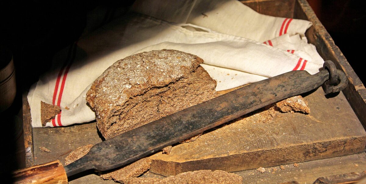 A round dark rye loaf on a cloth beside a long bread knife, in the Matterhorn Museum