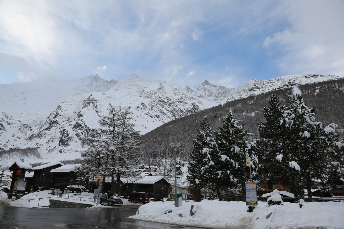 Snow-covered chalets and larches at the edge of Saas-Fee, with the peaks behind in winter