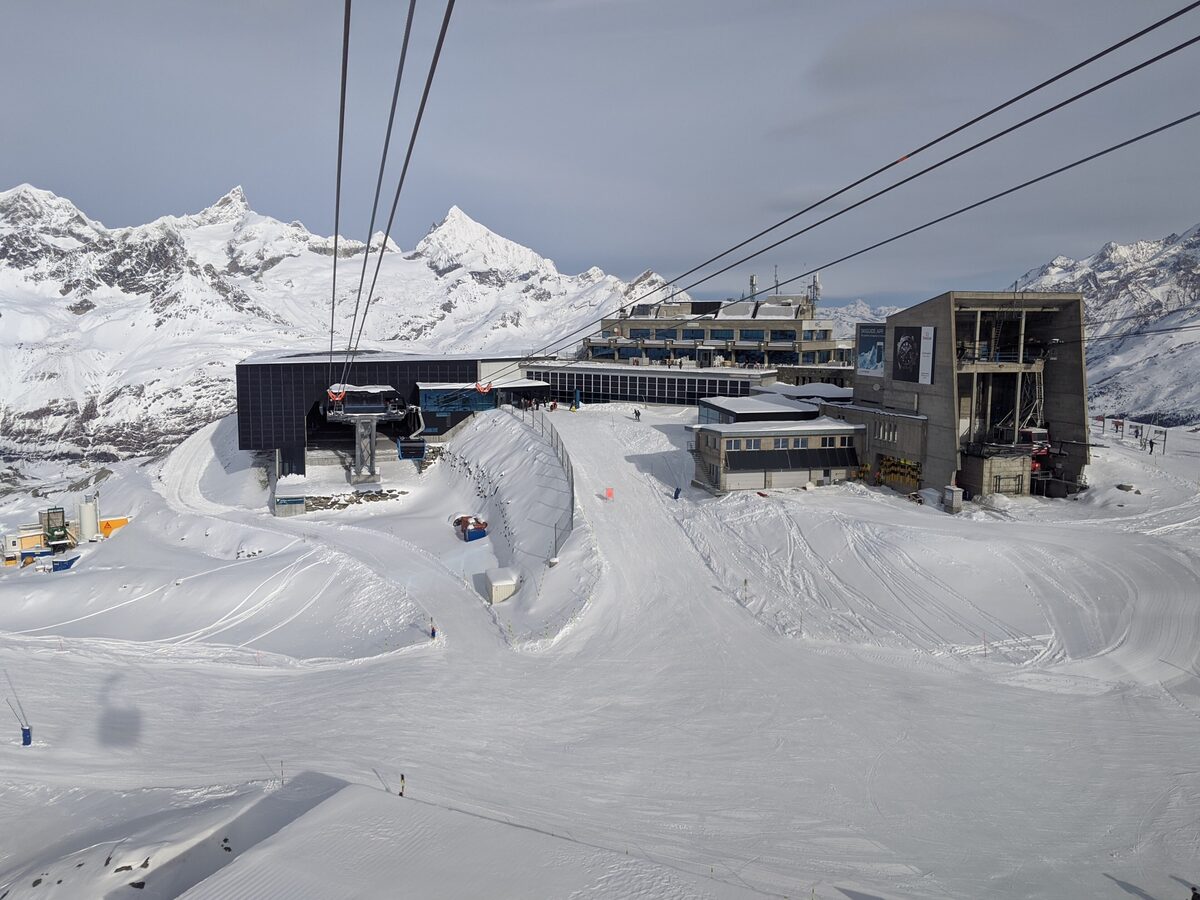 Cables running into the Trockener Steg station complex above snowy slopes, with peaks behind