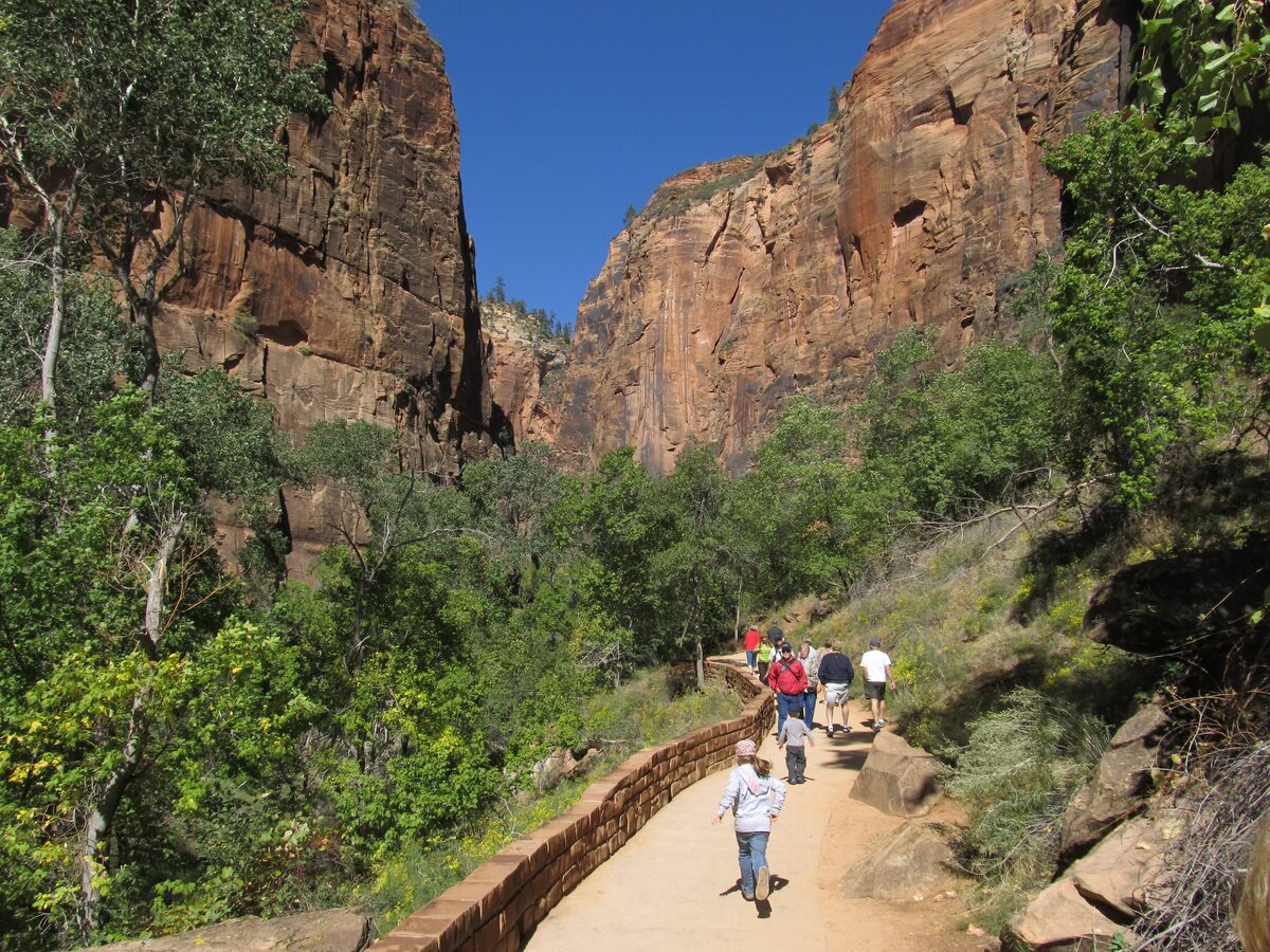 Hikers on the paved Riverside Walk between red cliffs and cottonwoods