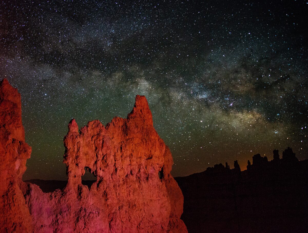 Milky Way over a lit hoodoo at night in Bryce