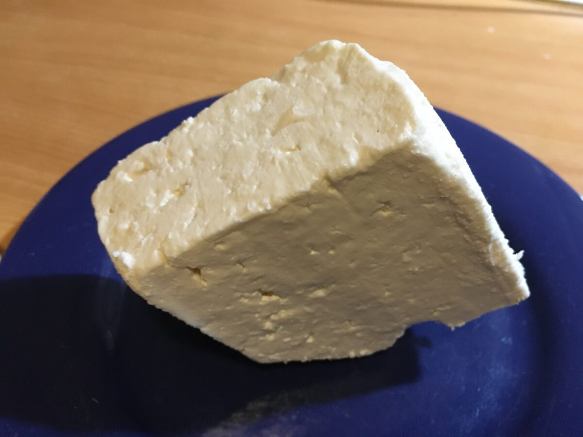 A thick wedge of white Zlatar cheese on a dark blue plate.