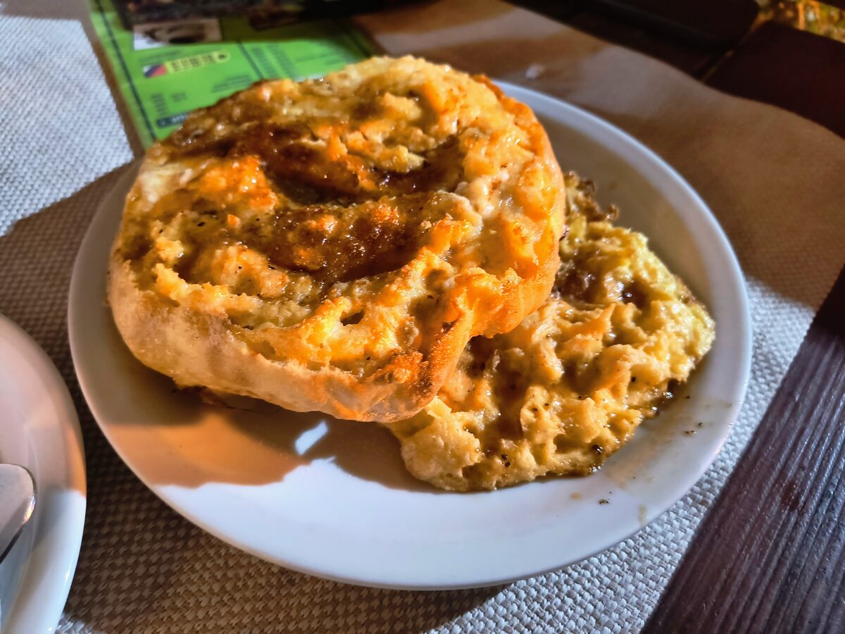 A komplet lepinja opened on a white plate, the round bread soaked with kajmak, egg and golden pretop.