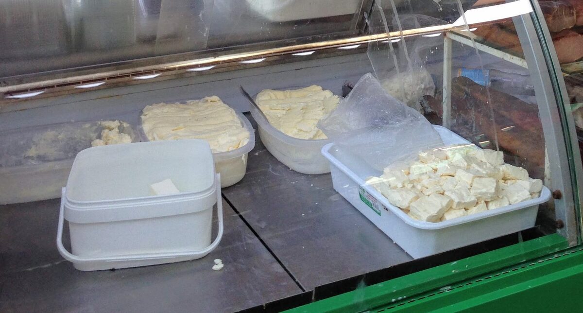 Tubs of creamy kajmak and a tray of white cheese cut into cubes in the glass counter of a market stall in the Užice area.