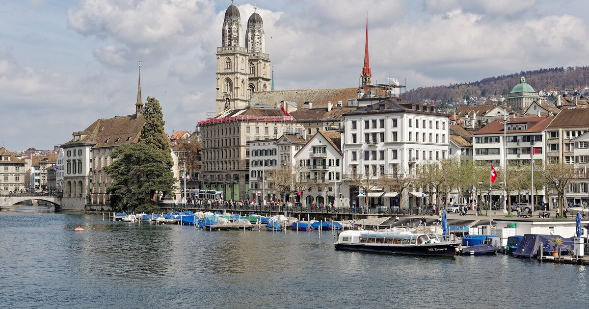 The Grossmünster towers and the old town above the Limmat, seen across the river from the lake end, with moored boats and a river boat in front