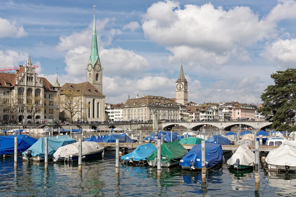 The green spire of the Fraumünster beside the Limmat, with moored boats in front and the St. Peter tower behind