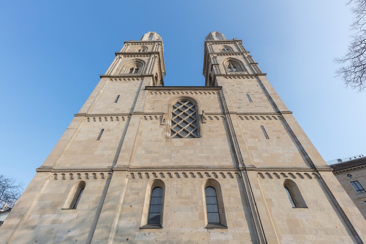 The two Romanesque towers of the Grossmünster rising against a pale blue sky, seen from below