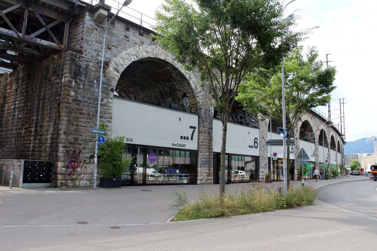 The stone railway viaduct arches on Viaduktstrasse, with shop fronts built into the arches and young trees in front