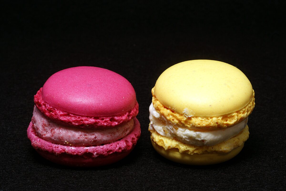 Two Luxemburgerli macarons, one raspberry pink and one yellow, on a black background