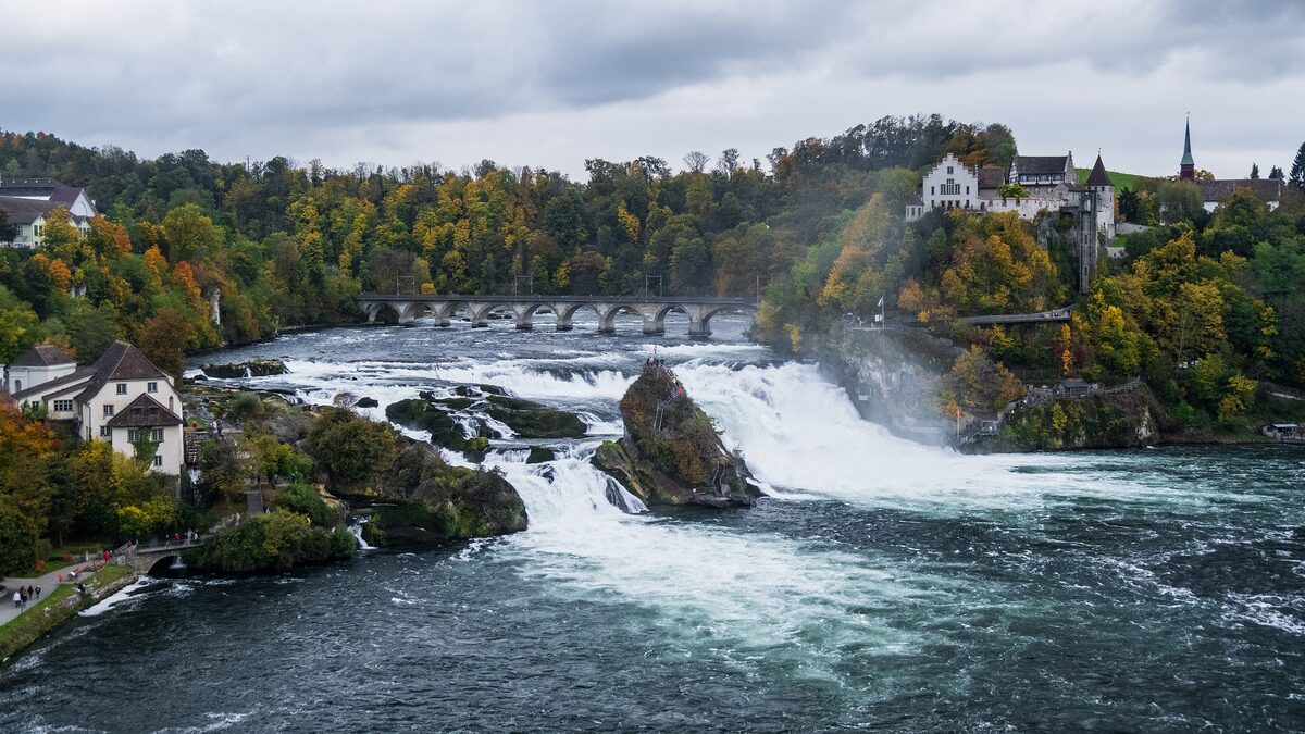 The Rhine Falls from the Neuhausen side, with the Middle Rock in the white water, Schloss Laufen on the cliff on the right and a railway bridge behind