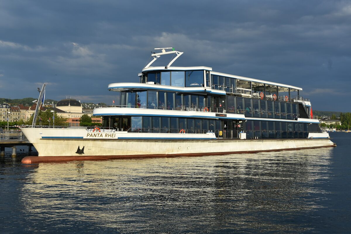 The two-deck lake ship Panta Rhei moored at the Bürkliplatz landing stage on Lake Zurich, with glass cabins and the shore behind